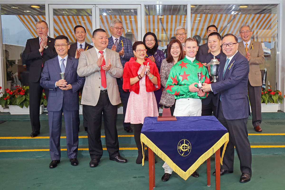 馬會董事廖長江先生於頒獎禮上將新馬錦標冠軍獎盃頒予「發財福星」馬主顏慶林先生及夫人、練馬師何良及騎師潘頓。