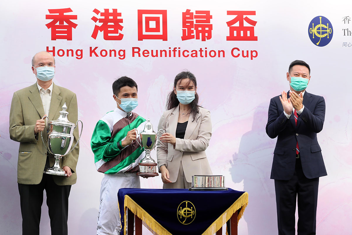 中央人民政府駐香港特別行政區聯絡辦公室宣傳文體部部長鄭琳女士（右），在「香港回歸盃」頒獎儀式上將紀念獎盃頒予「足金好球」的騎師潘明輝。