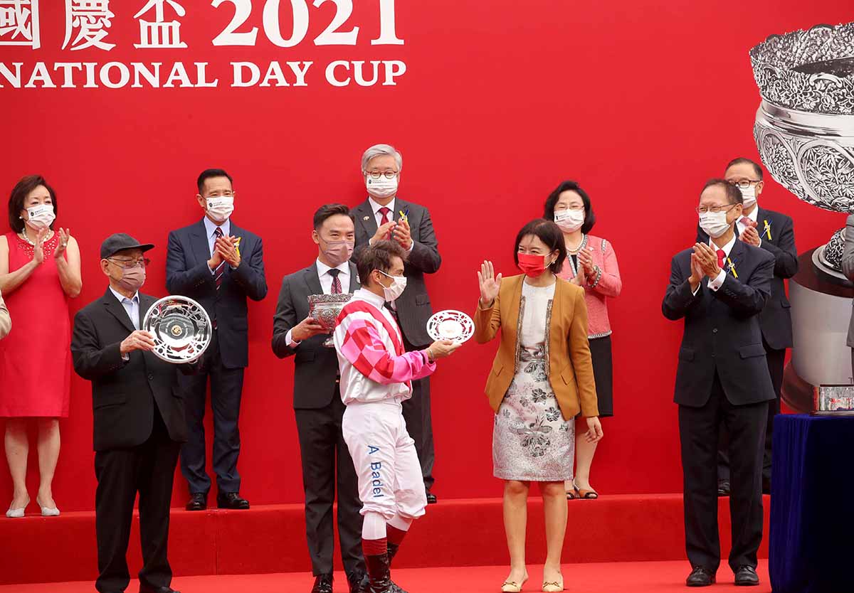 國慶盃頒獎儀式上，中央人民政府駐香港特別行政區聯絡辦公室副主任盧新寧女士頒發銀碟予勝出馬匹「聚才」的練馬師大衛希斯及騎師巴度。
