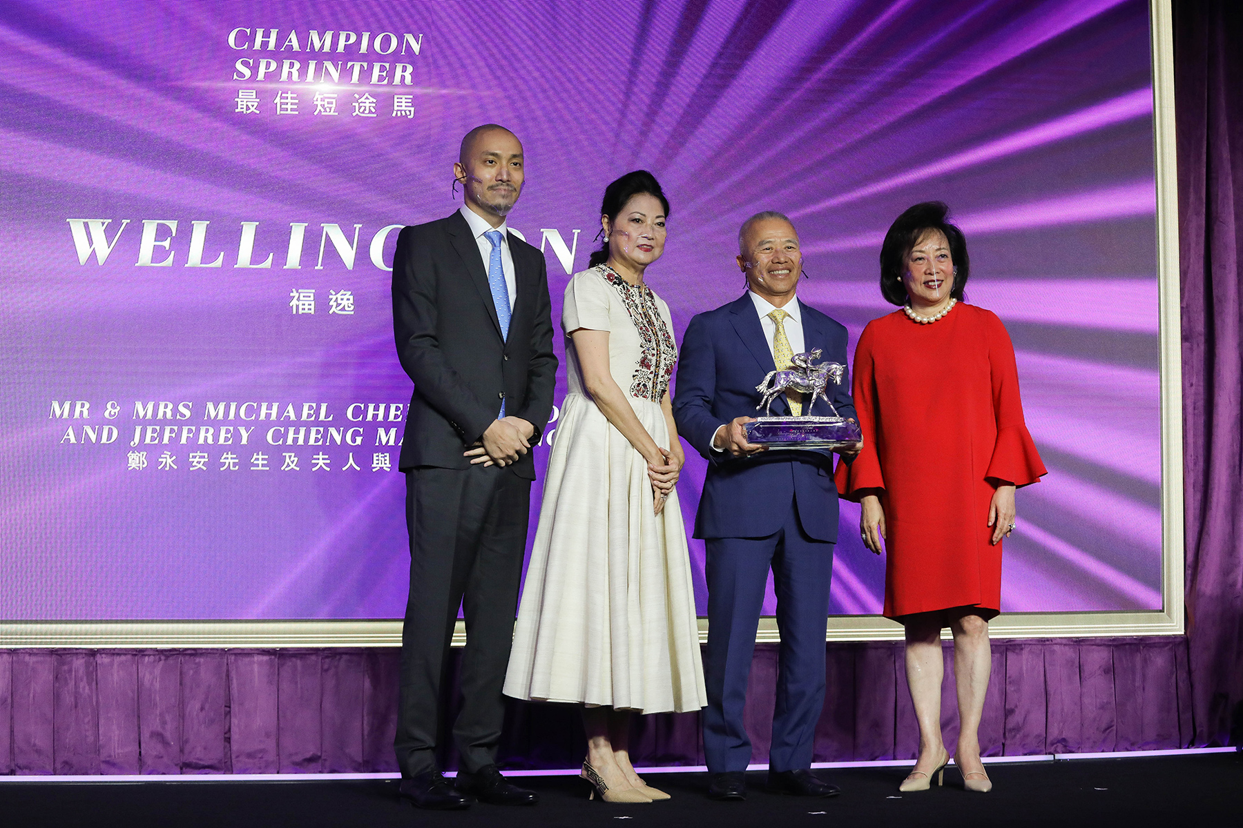 香港賽馬會董事王䓪鳴博士頒發最佳短途馬獎座予「福逸」的馬主鄭永安先生及夫人與鄭文昌先生。