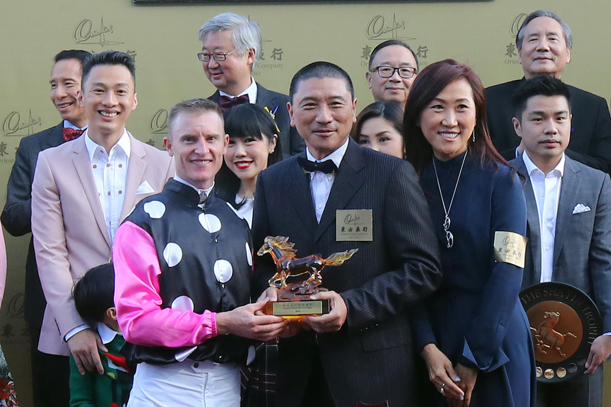 Executive Director of the Oriental Watch Holdings Limited Mr. Alain Lam Hing Lun, accompanied by his wife, presents a souvenir to jockey Zac Purton.
